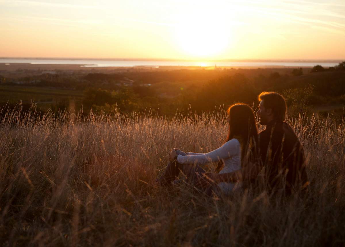 St. Margarethen Quarry: Admission + Guided Tour Two people sitting in a grassy field, facing a sunset over a distant landscape and water.