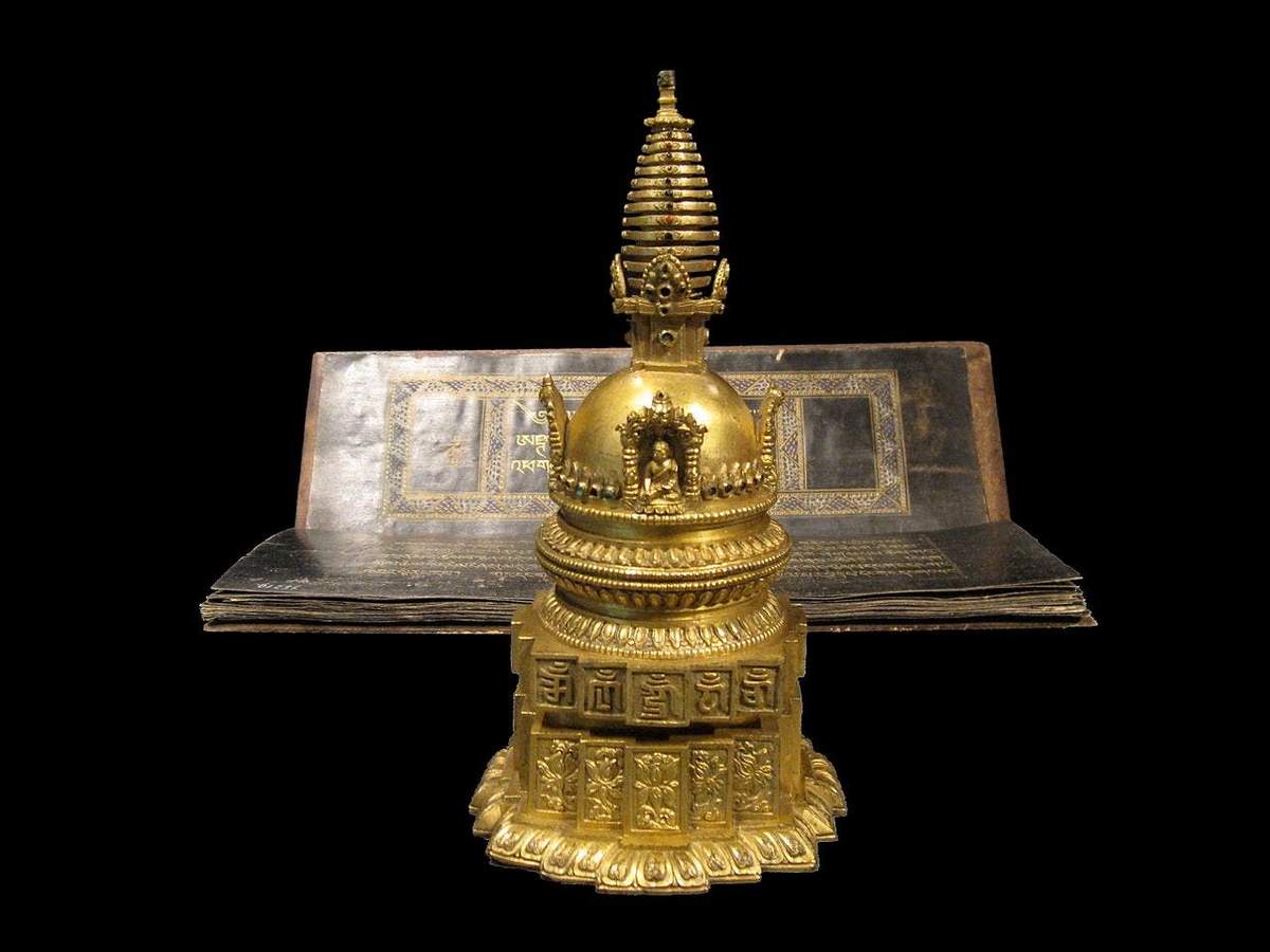 Weltmuseum: Skip The Line Ticket A golden stupa with intricate details is positioned in front of an open, ornate book, set against a black background.