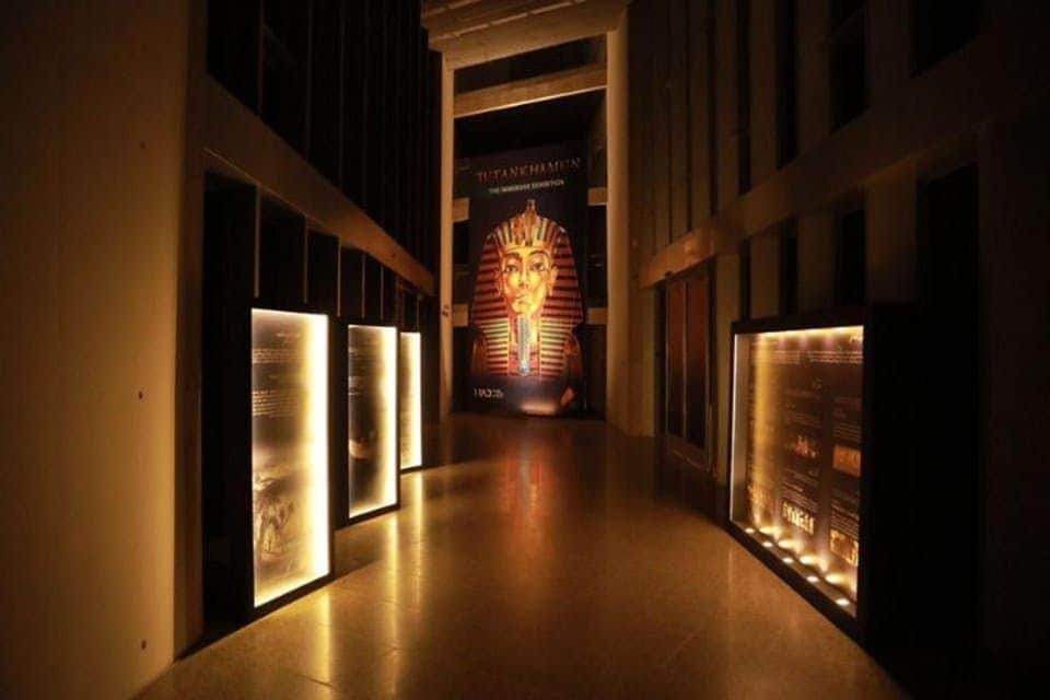 Grand Egyptian Museum: Skip The Line Ticket Dimly lit hallway with illuminated display panels and a large image of Tutankhamun's mask at the end.