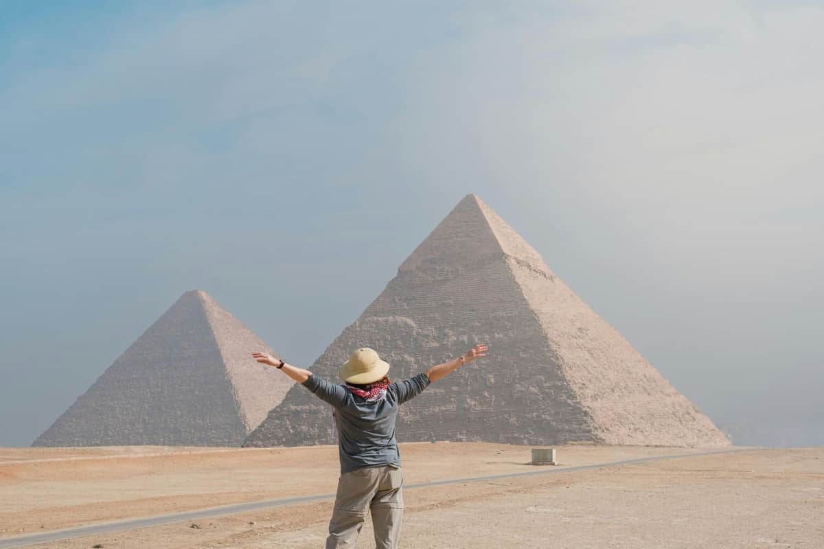 Pyramids of Giza and Sphinx Tour with Nile River Felucca Ride Person with outstretched arms facing the pyramids of Giza on a clear day.
