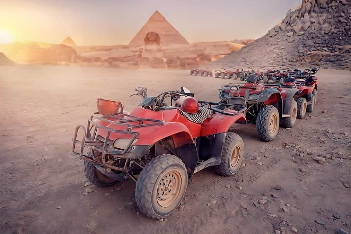 Pyramids of Giza: Skip The Line Ticket + Quad or Camel Ride + Transfers Several red all-terrain vehicles parked on a desert landscape with pyramids and rocky surroundings in the background.