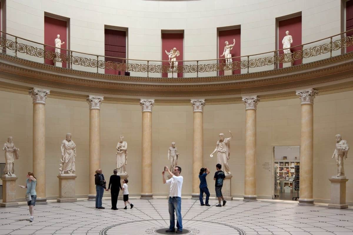 Altes Museum: Entry Ticket A gallery with statues and columns, visitors observing and taking photos, featuring a circular layout and upper level statues.