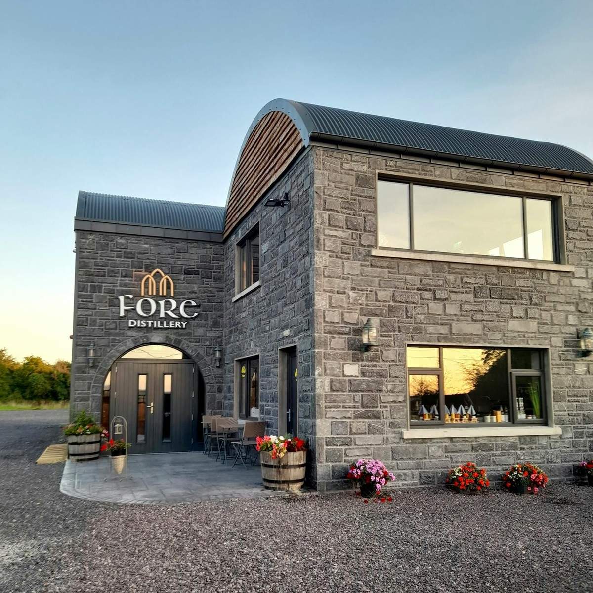 Celtic Boyne Valley & Ancient Sites: Day Tour from Dublin A stone building labeled "Fore Distillery" with large windows, outdoor seating, potted plants, and a gravel pathway.