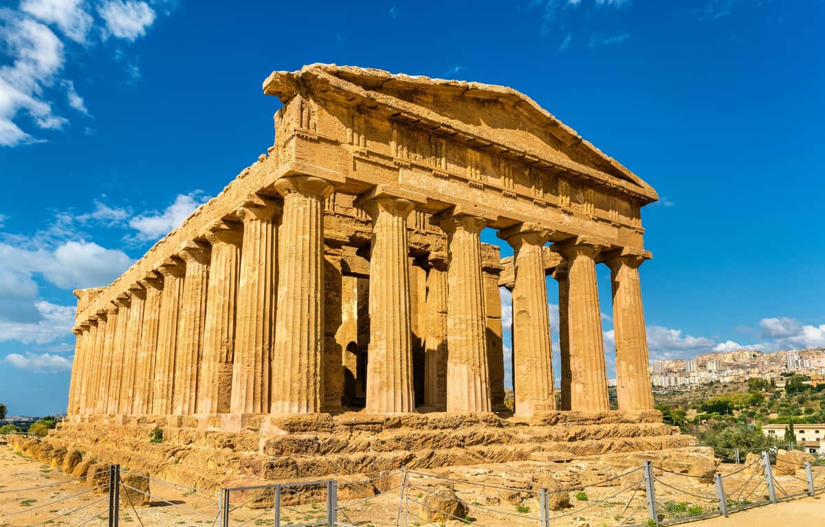 Ancient Greek temple with tall, weathered columns and a triangular pediment under a clear, blue sky.