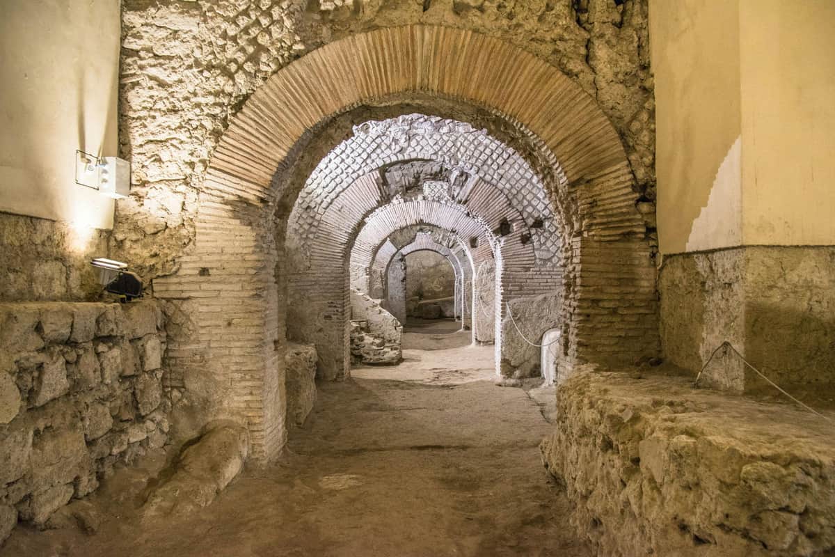 Complex of San Lorenzo Maggiore & Archaeological Area: Entry + Audio Guide Ancient stone ruins with multiple arches, brick and stone masonry, dusty floor, and ambient light highlighting the structure.