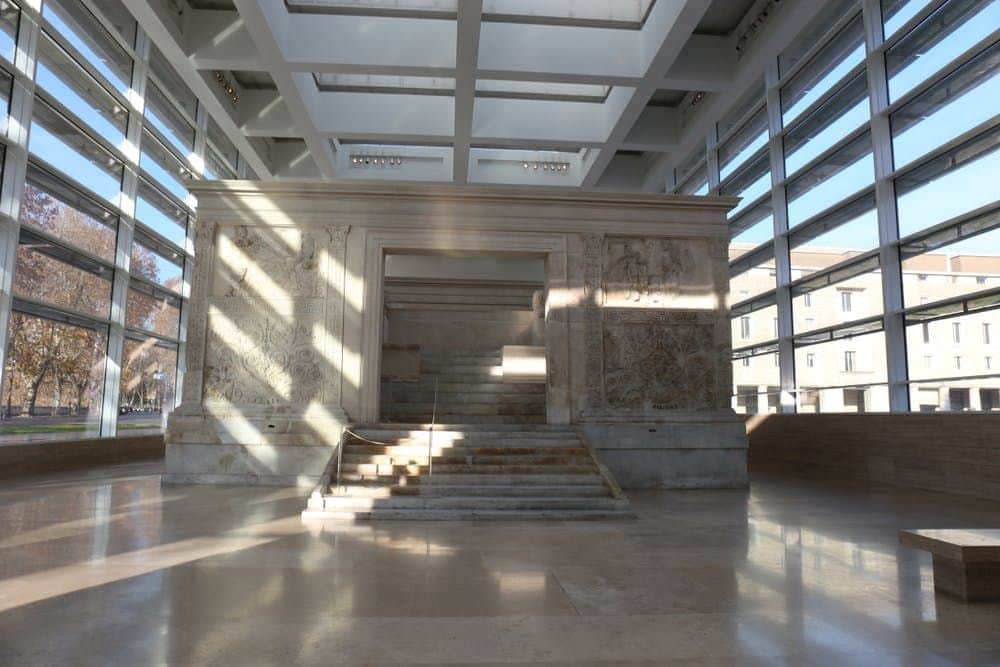 Ara Pacis Museum: Entry Ticket An ancient stone structure with intricate carvings, set in a modern glass and steel building with large windows and skylights.