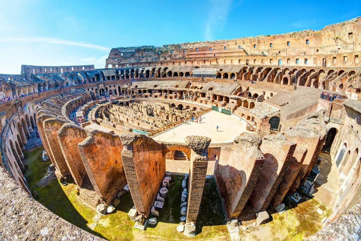 Colosseum & Roman Forum + Audio Guide Interior view of the Colosseum in Rome, showing ancient stone architecture, tiered seating, and a partially restored arena floor.