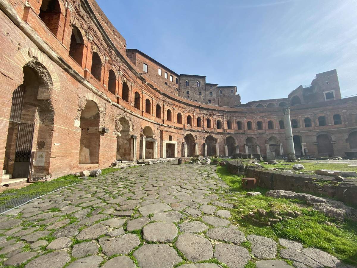 Ancient Roman brick ruins with arched openings and a cobblestone pathway under a clear blue sky.