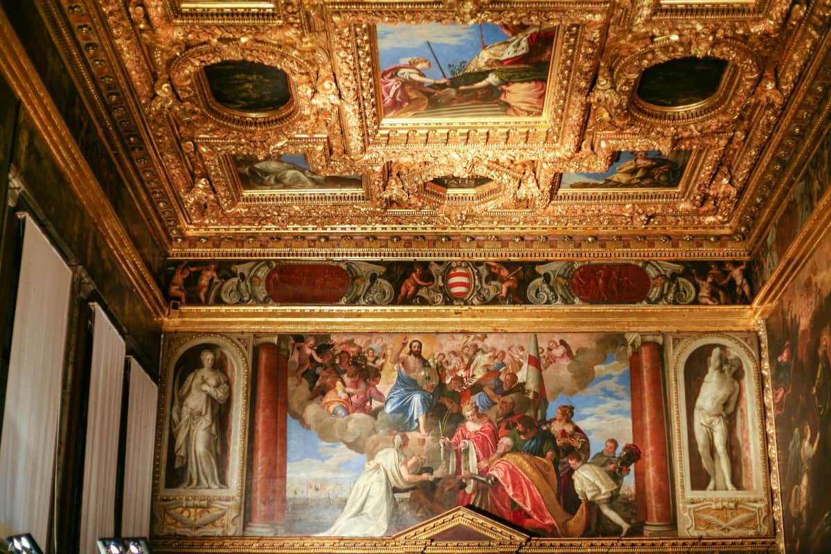 Ornate room with a gold, intricately decorated ceiling and large mural depicting a biblical scene with multiple figures.