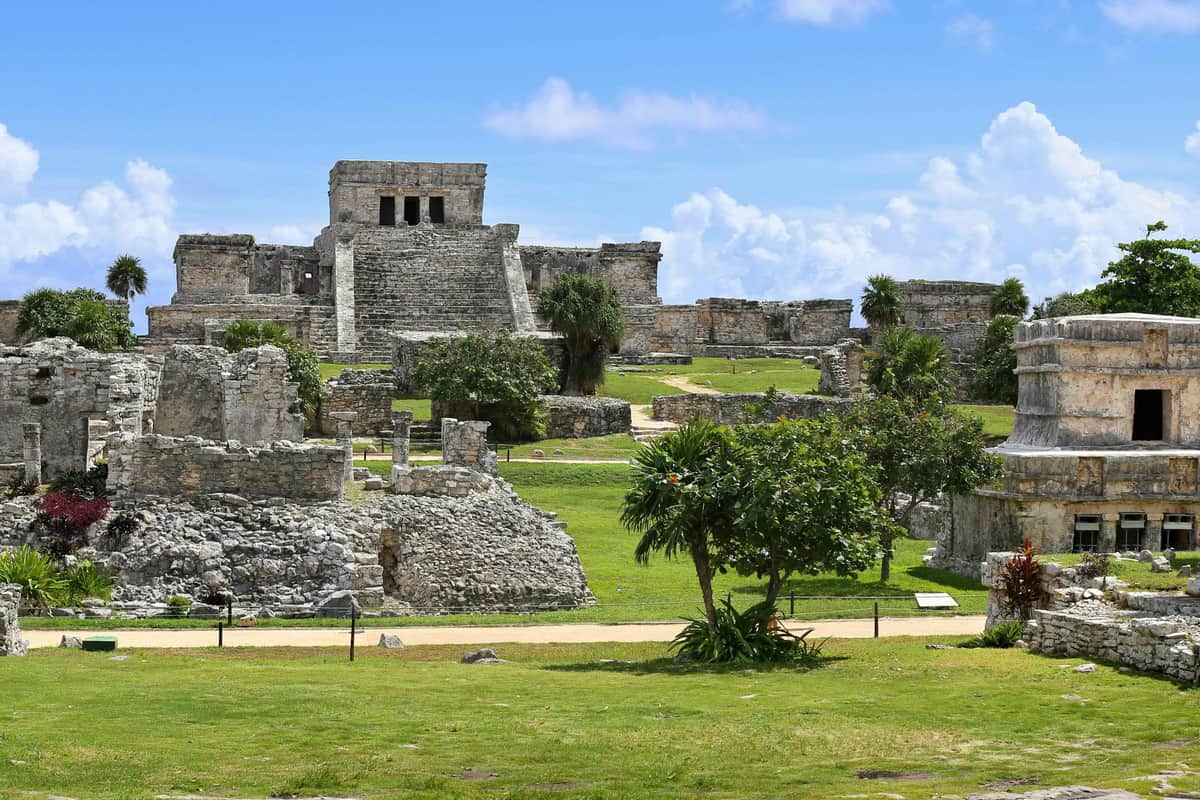 Tulum, Cenote Mariposa & Chen Ha: Guided Tour + Transport Ancient stone ruins with steps and lush green grass under a bright blue sky with scattered clouds.