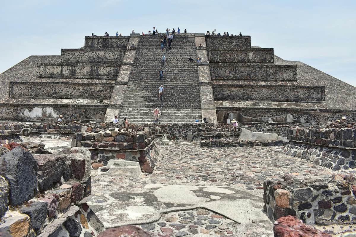 Teotihuacán Pyramids & Shrine of Guadalupe: Day Tour with Lunch People climb the large, ancient stone pyramid steps at Teotihuacan, surrounded by ruins under a clear sky.