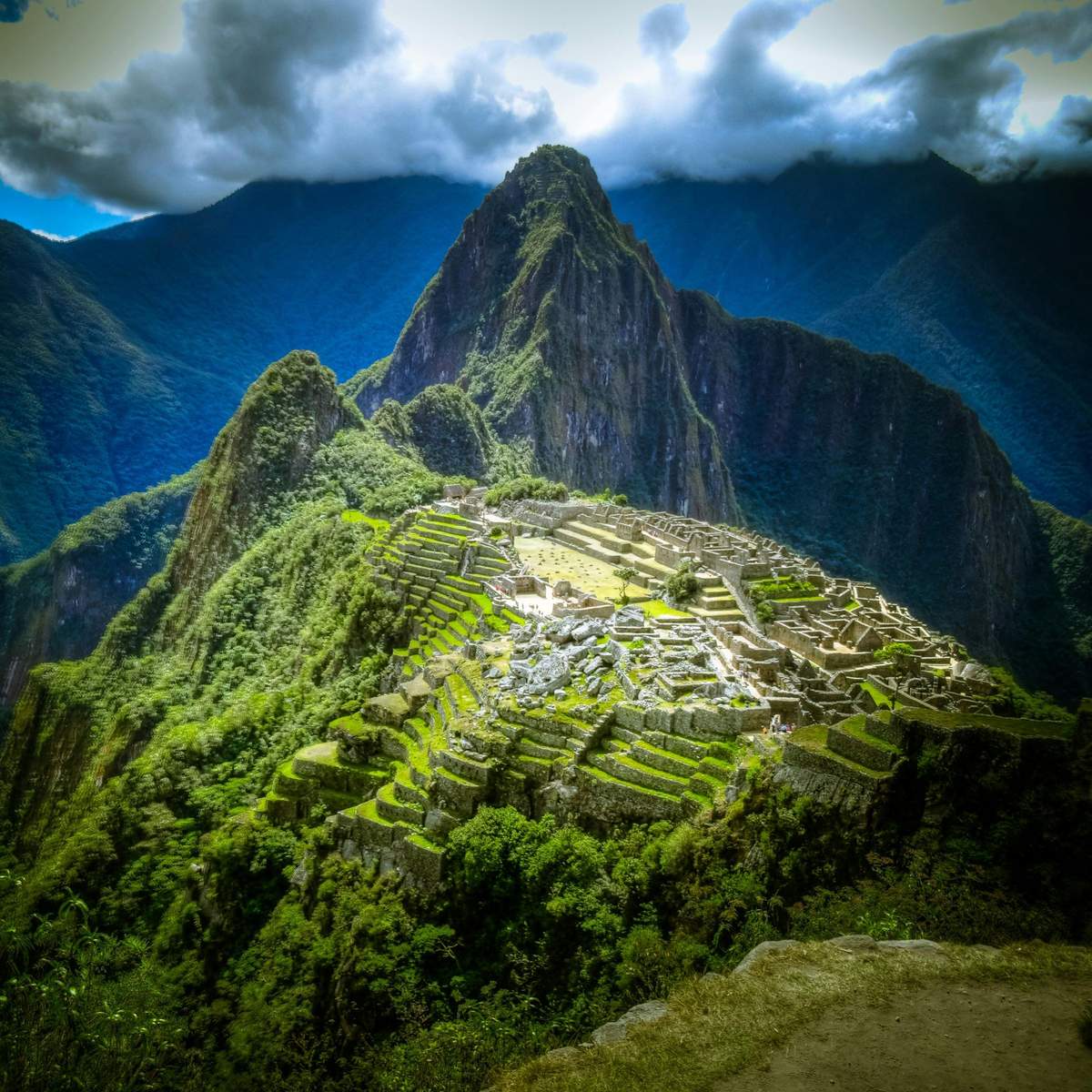 Machu Picchu: Entry Ticket + Guided Tour Ancient ruins of Machu Picchu nestled among lush, green mountains under a cloudy sky.