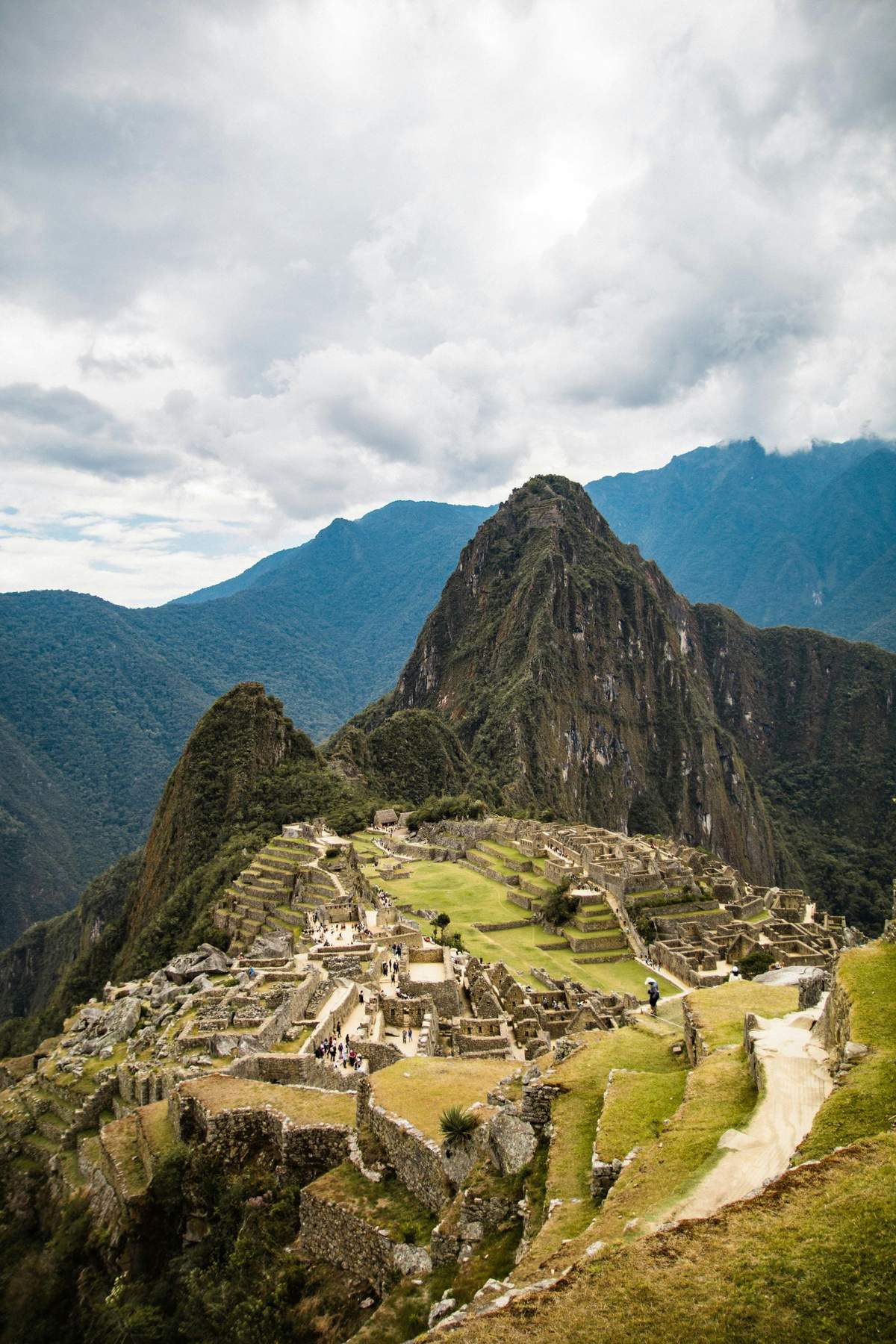 Machu Picchu: Entry Ticket Ancient Incan ruins of Machu Picchu with terraces and stone structures, set against tall, green mountains under a cloudy sky.