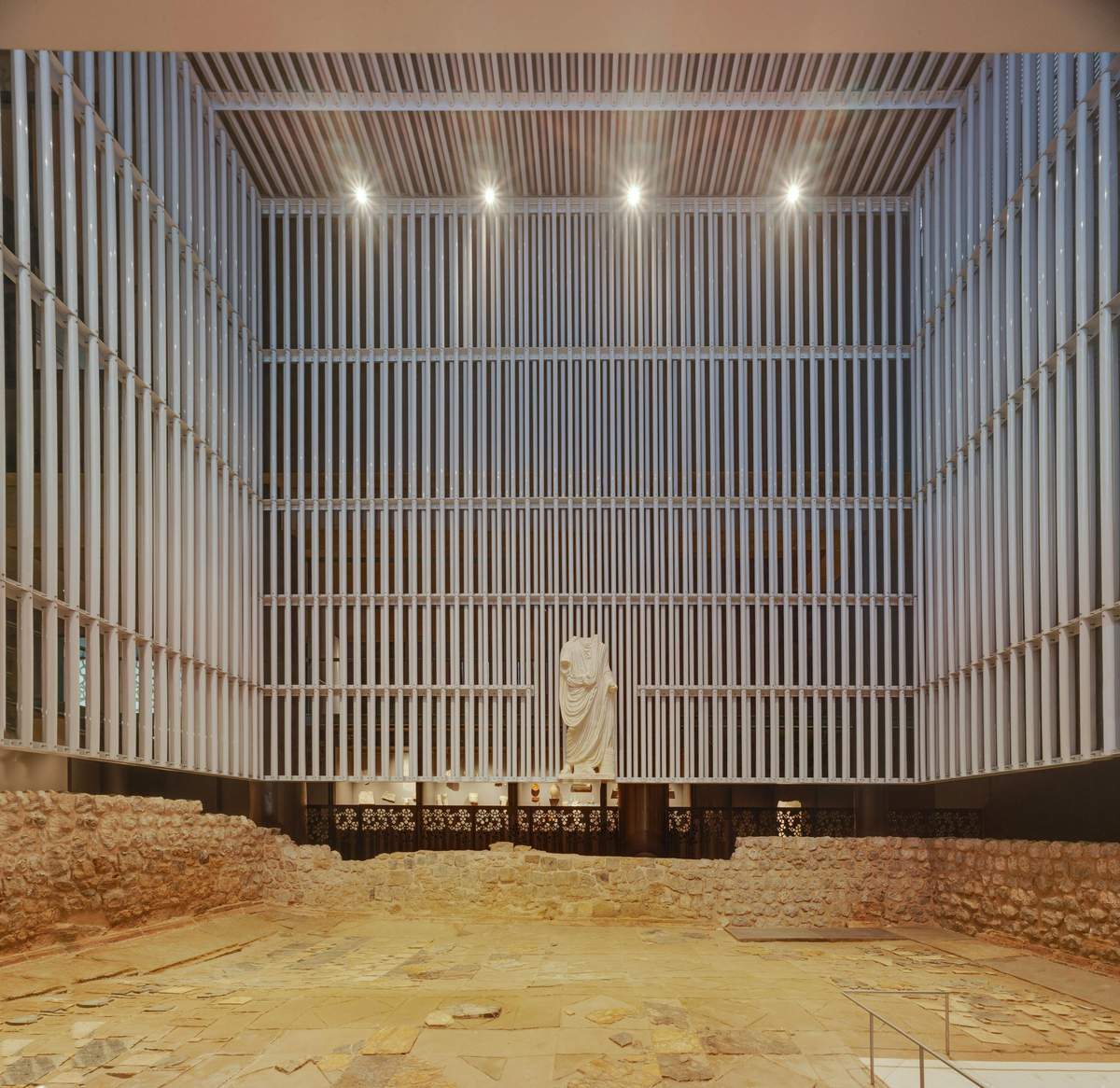 Roman Forum Museum Molinete Indoor archaeological exhibit featuring ancient ruins and a prominent white statue, illuminated by ceiling lights.