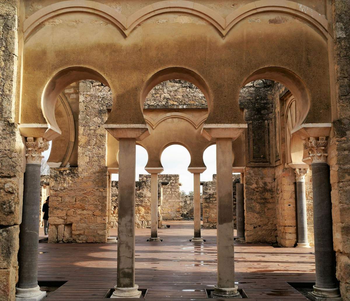 Medina Azahara: Guided Tour Stone arches and columns in a historical ruin, with intricate detailing and a partially open roof.