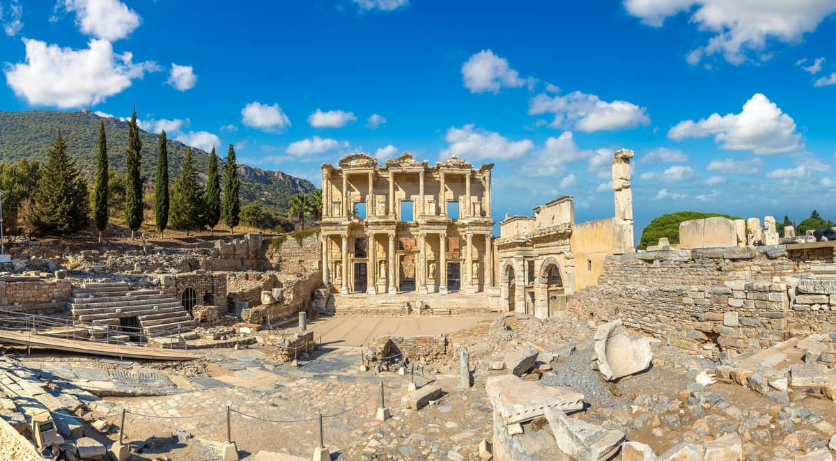 Ephesus Day Tour from Izmir Ancient Roman ruins with a partially intact two-story structure, scattered stones, and clear blue sky in the background.