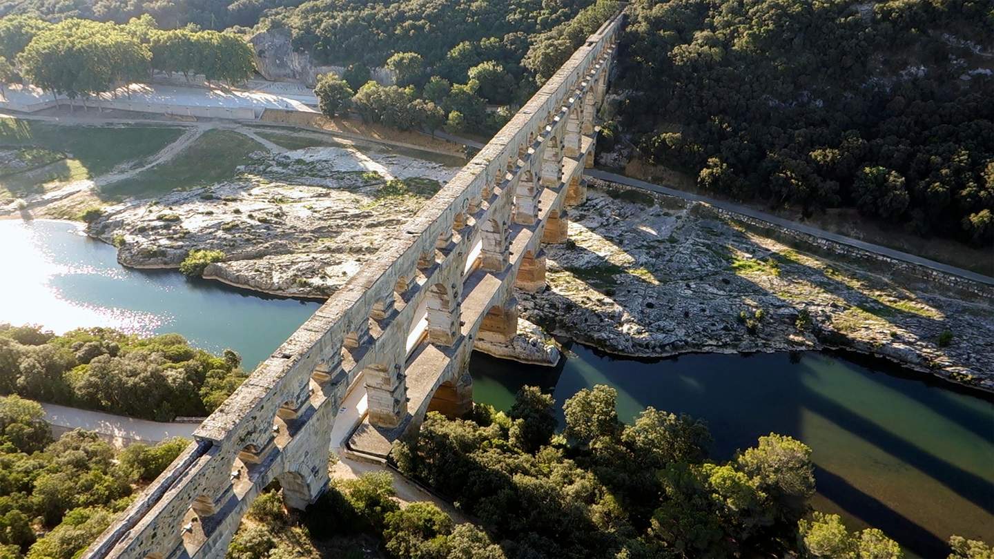 Pont du Gard Ancient stone aqueduct with arches spanning over a river, surrounded by rocky terrain and forested area.