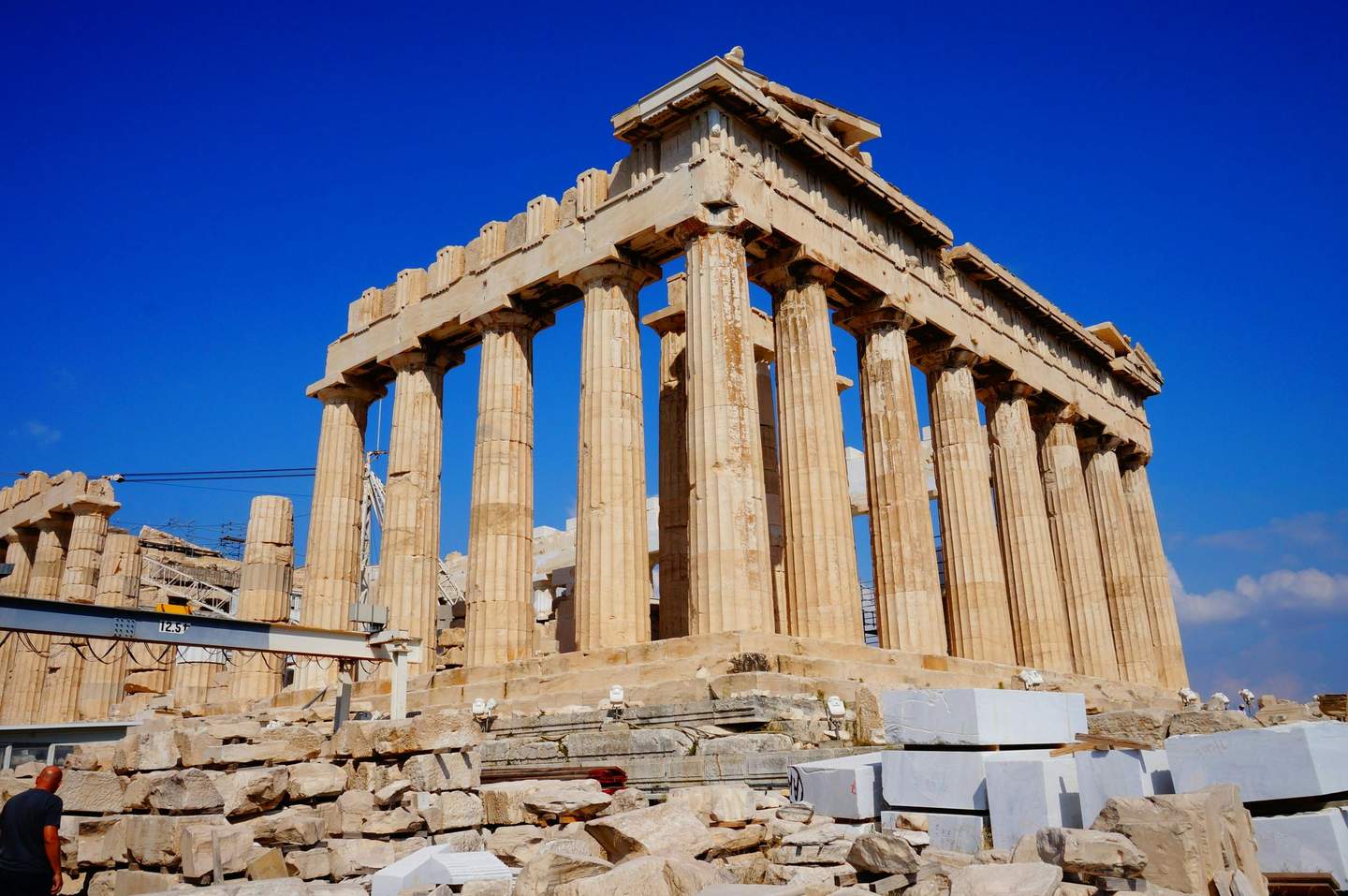 Acropolis of Athens Ancient Greek temple with tall columns and scaffolding for restoration under a clear blue sky; scattered stones in the foreground.