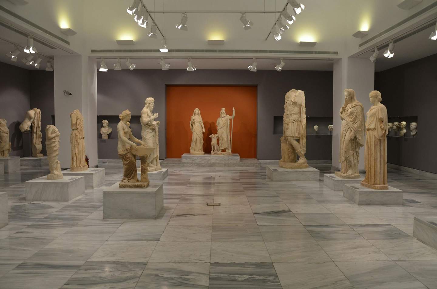 Heraklion Archaeological Museum A museum gallery with various classical statues and busts displayed on marble pedestals under bright ceiling lights.