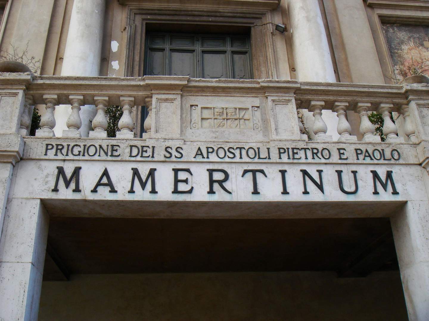 Mamertine Prison A stone entrance with a balustrade above it, featuring the text "PRIGIONE DEI SS APOSTOLI PIETRO E PAOLO MAMERTINUM."