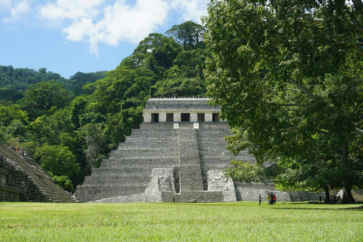 Archäologische Stätte von Palenque Ticket (Cancún) Eine alte Steinpyramide, umgeben von üppig grünen Bäumen, im Vordergrund stehen einige Menschen unter einem großen Baum.