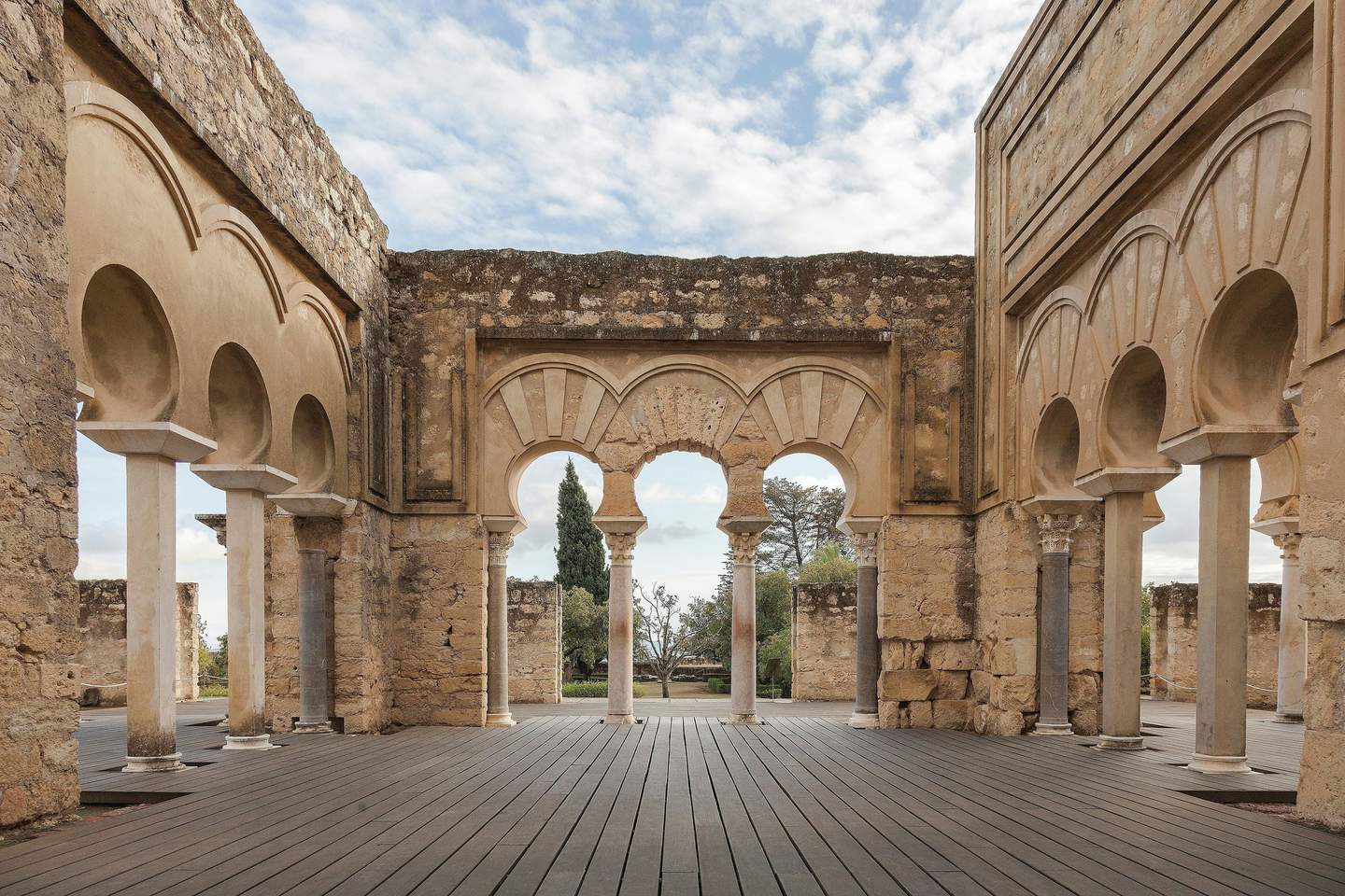 Ancient stone structure with arched columns, part of a ruin, featuring a courtyard and a clear sky in the background.