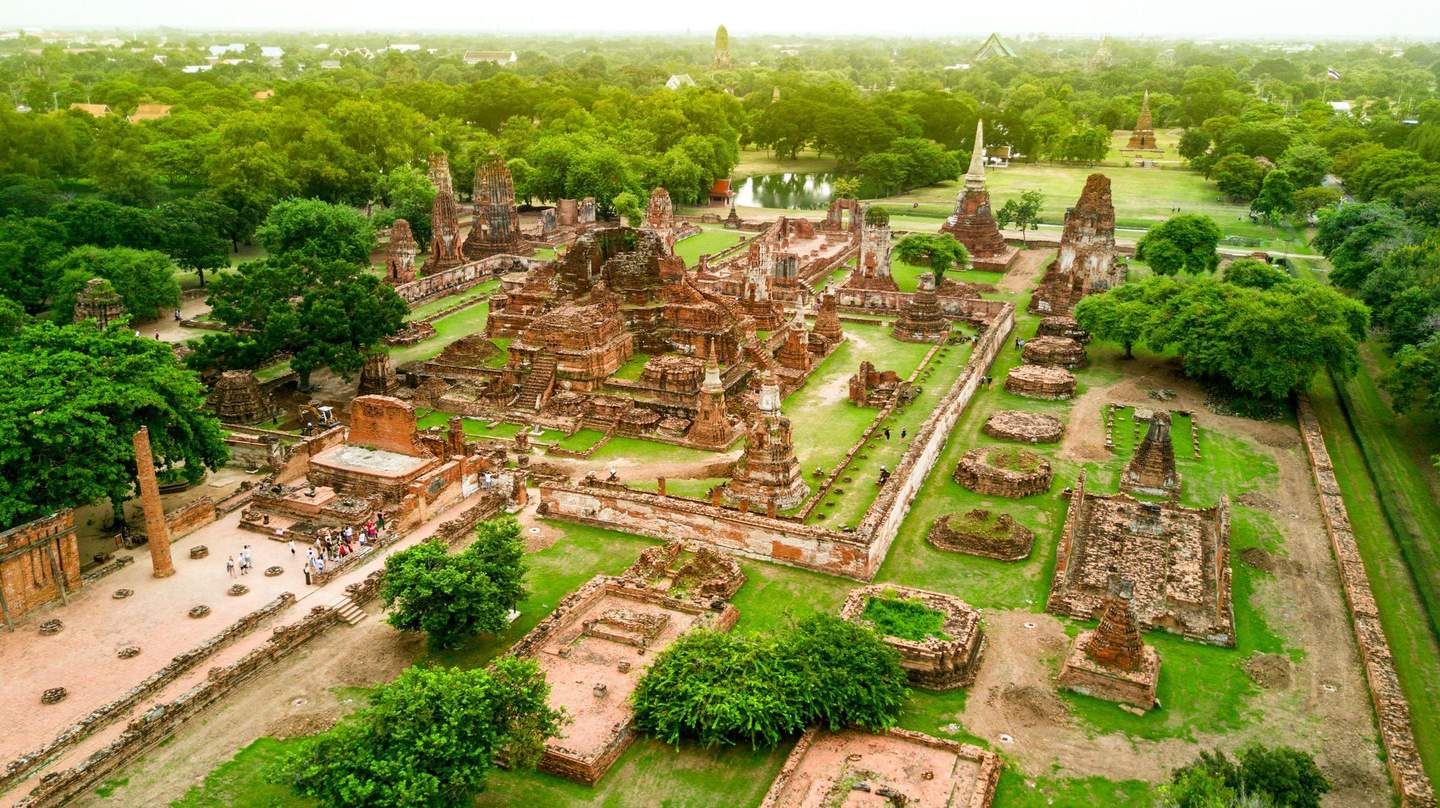 Aerial view of ancient temple ruins surrounded by lush greenery and trees, with scattered visitors exploring the site.