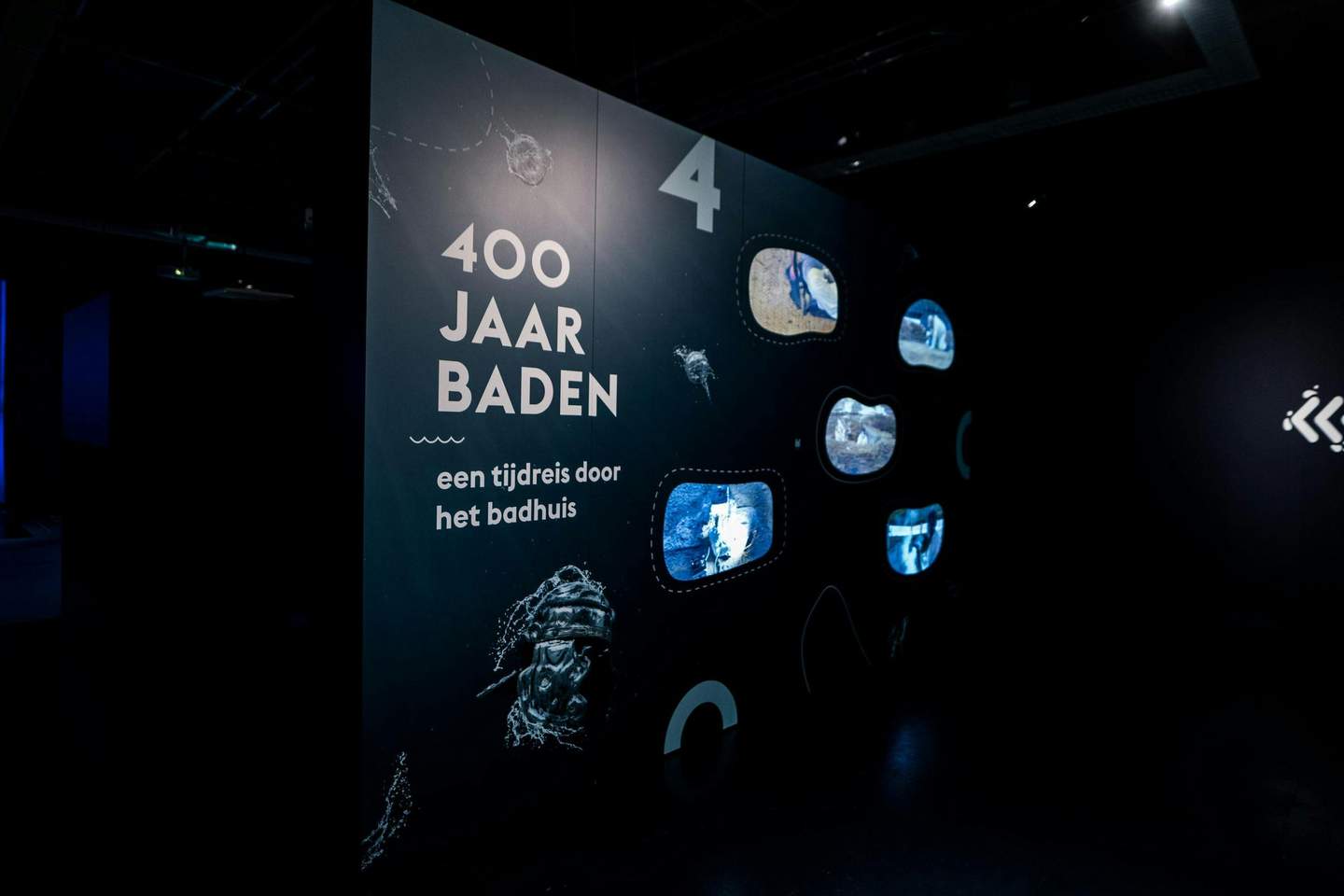 Thermenmuseum Dark exhibition panel with "400 Jaar Baden" text alongside six small display screens showing various water-themed visuals.