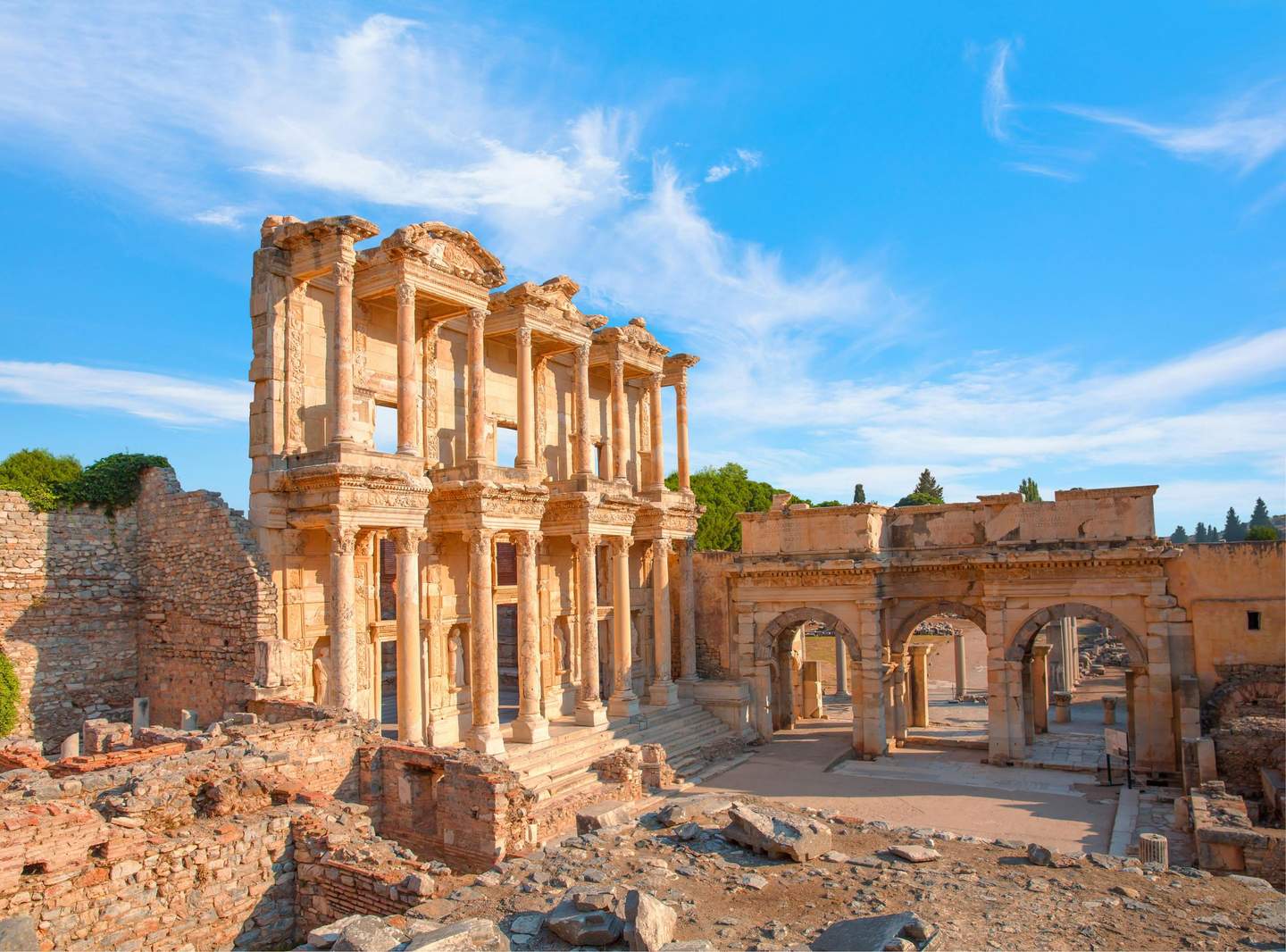 Library of Celsus in Ephesus Ancient stone ruins with intricate columns and arches under a bright blue sky, surrounded by scattered rocks and partial walls.