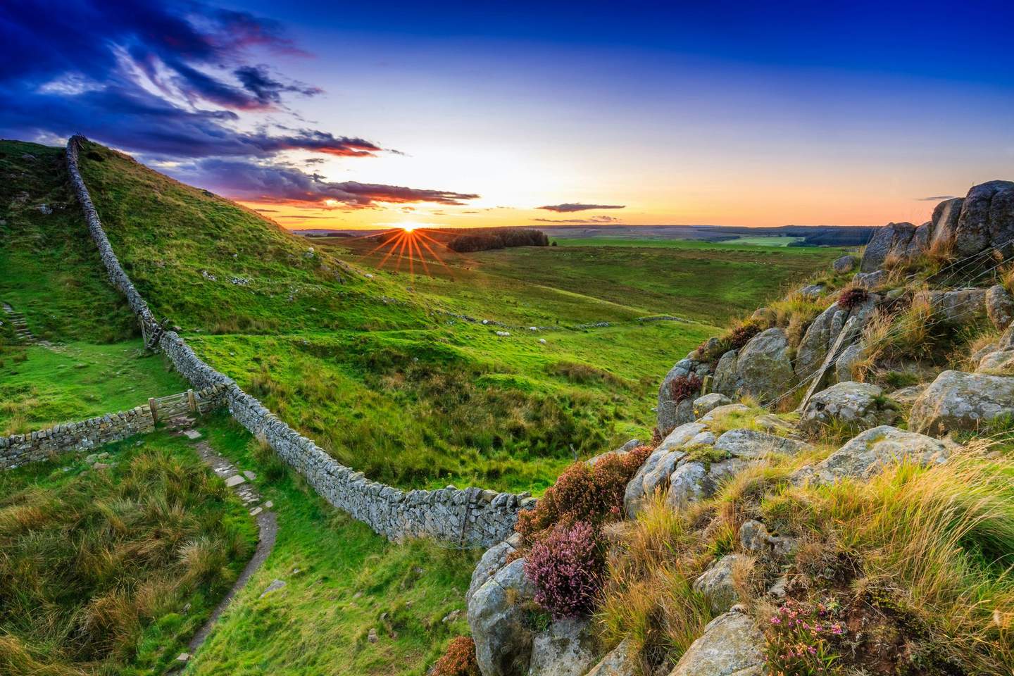 Hadrian's Wall A stone wall spanning a green landscape at sunset, with sunlight casting a warm glow over fields and hills.
