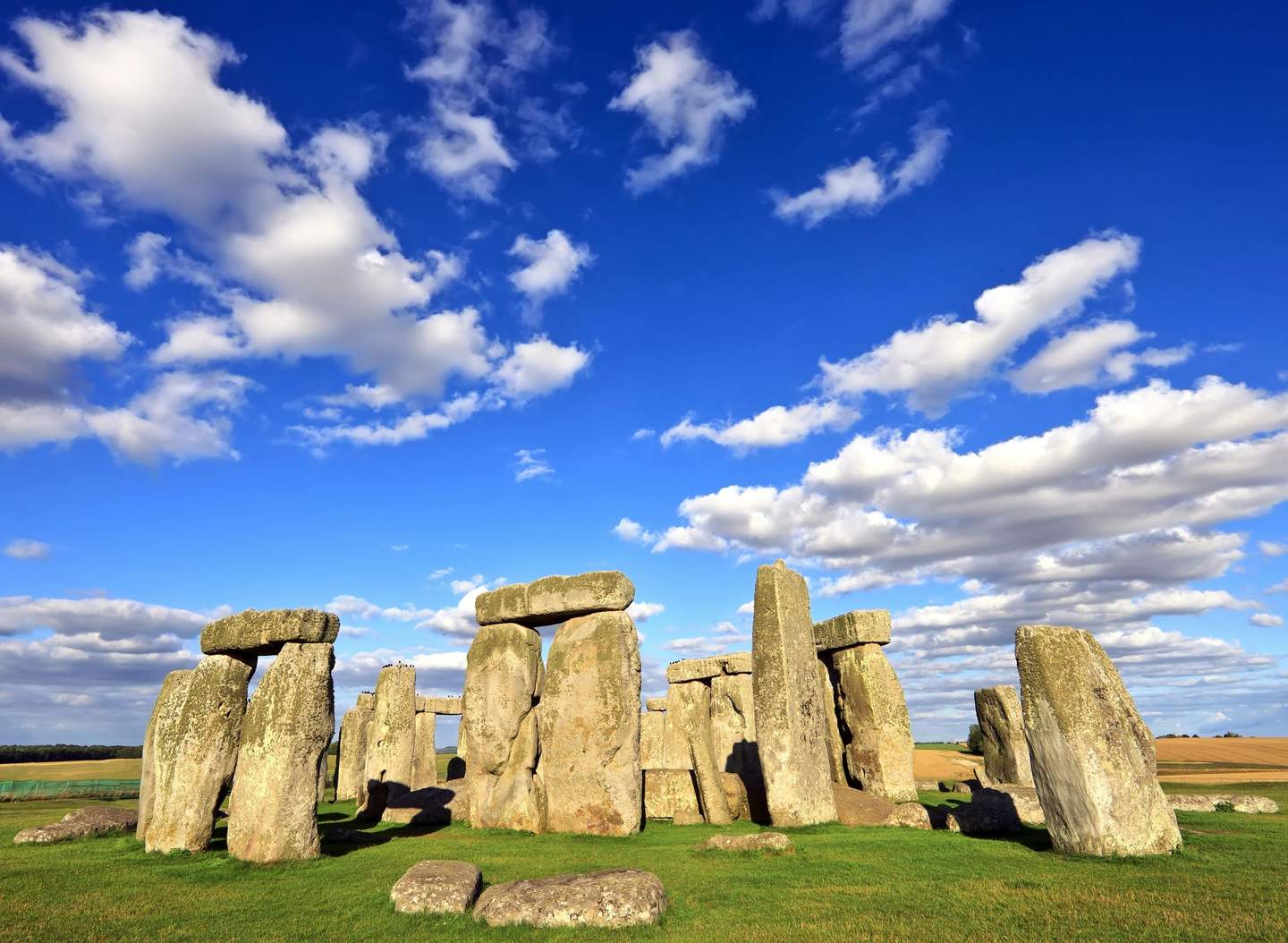 Stonehenge Ancient stone structure at Stonehenge on grassy field under a blue sky with scattered white clouds.