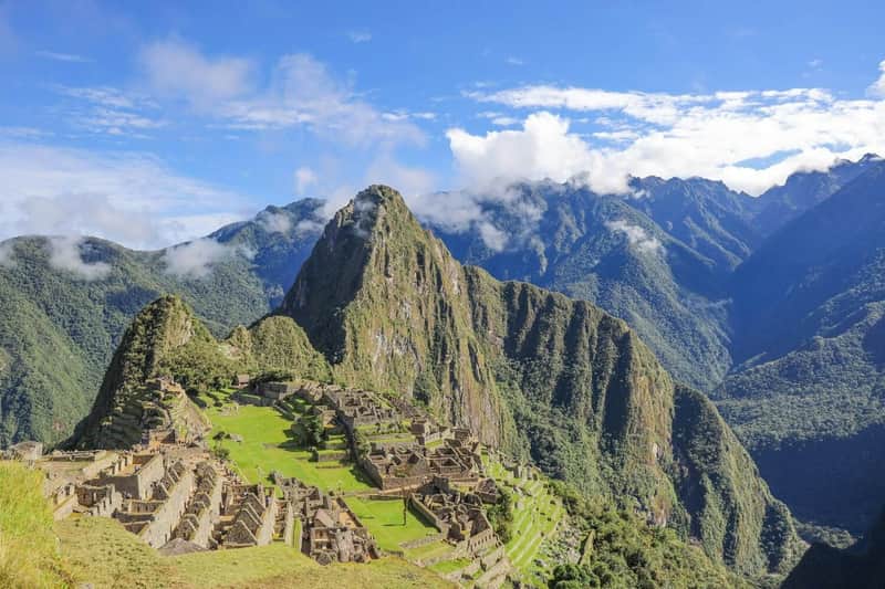Machu Picchu: Circuit 1A - Mountain Route Ticket A panoramic view of Machu Picchu ruins surrounded by green mountains and a blue sky with clouds.