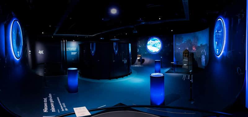 Thermenmuseum: Entry Ticket + Audio Guide A dimly lit exhibition space with blue lighting, cylindrical displays, a large black structure, and a circular illuminated screen.