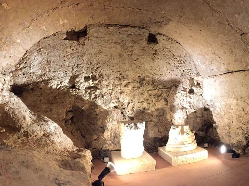 Termoli Underground A stone-walled room with two broken pillars on the floor, illuminated by spotlights.