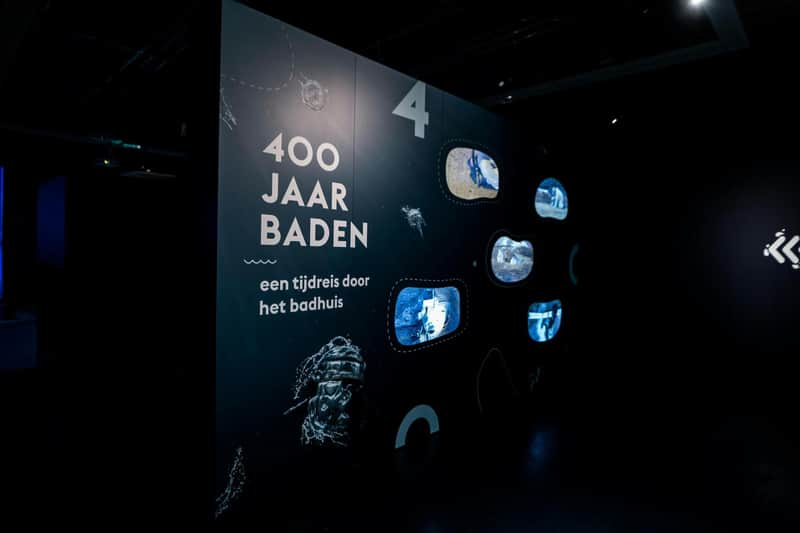 Thermenmuseum Dark exhibition panel with "400 Jaar Baden" text alongside six small display screens showing various water-themed visuals.