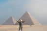 Person with outstretched arms facing the pyramids of Giza on a clear day.