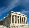 Ancient stone temple with tall columns and scaffolding, set against a bright blue sky with scattered clouds.