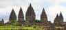 Prambanan Temple Several ancient, intricately carved stone temple towers rise above a grassy area with scattered ruins.
